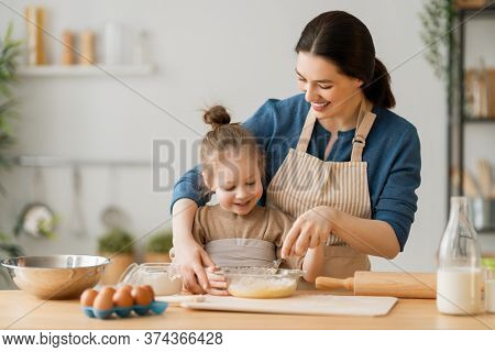 Happy loving family are preparing bakery together. Mother and child daughter girl are cooking cookies and having fun in the kitchen. Homemade food and little helper.   