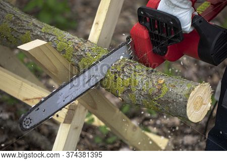 Man Sawing Wood With A Chain Saw Using Sawhorse Close Up Domestic Work. Chainsaw Sawn A Timber. Hand