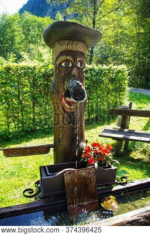 Hallstatt, Austria, 08.31.2011. Street Standpipe In The Form Of A Wooden Man In A Hat. The Water Flo