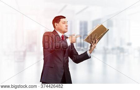 Senior Businessman Finger Pointing Into Open Book. Portrait Of Adult Man In Business Suit And Tie St