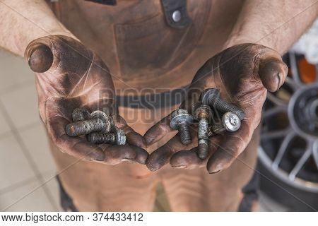 Auto Mechanic in dirty clothes holds bolts in hands stained with oil