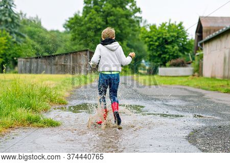 Happy Kid Boy Wearing Red Rain Boots And Walking During Sleet And Rain On Rainy Cloudy Day. Child In