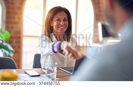 Two middle age business workers smiling happy and confident. Working together with smile on face using laptop doing handsake at the office