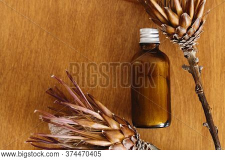 Herbal Organic Ubtan In Glass Bottle On Wooden Background With Dried Protea Flowers, Flat Lay. Ubtan