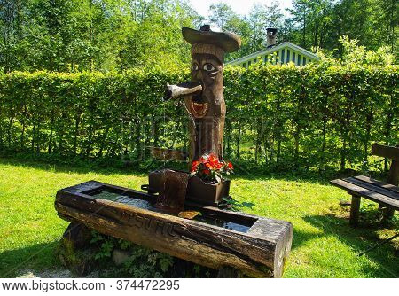 Hallstatt, Austria, 08.31.2011. Street Standpipe In The Form Of A Wooden Man In A Hat. The Water Flo