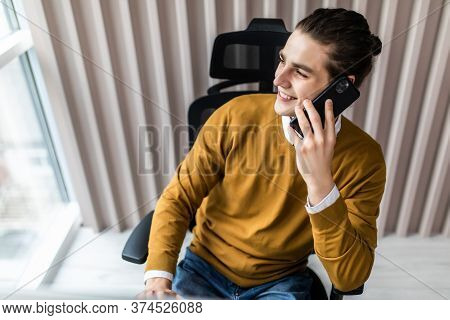 Portrait Of Smiling Businessman Speaking On Mobile Phone, Sitting At Desk, Looking At Computer Scree