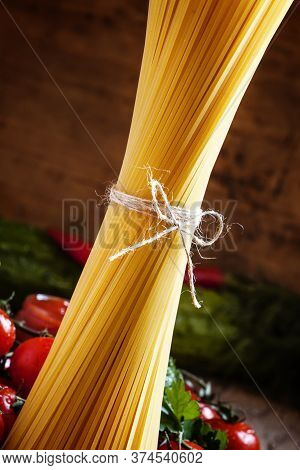 Italian Dry Pasta Spaghetti With Tomatoes And Fresh Herbs On A Dark Wooden Background, Selective Foc