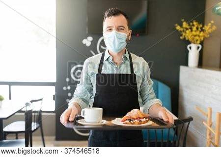 Portrait Of Waiter Wearing Face Mask While Serving Order In Coffee Shop