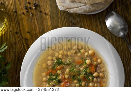 Top View Vegetarian Thick Cheakpea Soup With Corrots And Greens In White Plate On Served Wooden Tabl