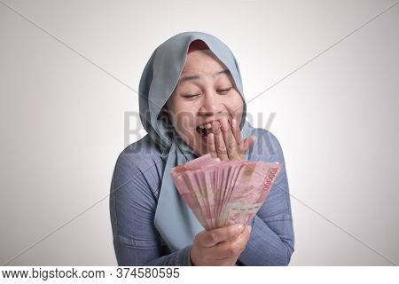 Portrait Of Indonesian Muslim Woman Holding Rupiah Money, Smiling Laughing Winning Gesture
