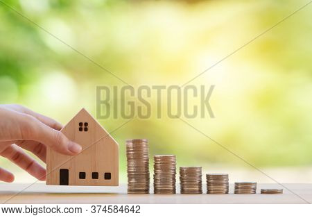 Hand Holding Wooden House Model And Stack Of Cions On Wooden Panel Nature Green Background, Concept 