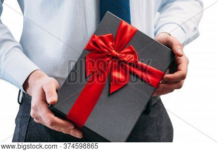 Business Man Holding A Gift With A Red Ribbon. Guy On A White Background In A Light Shirt With A Tie