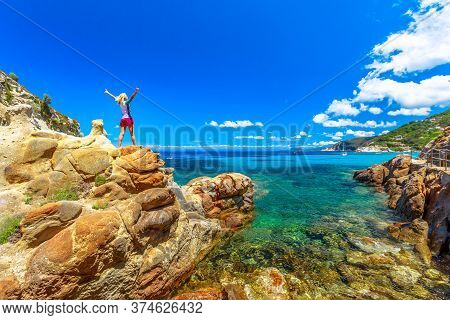 Happy Woman In Diving Suitdress With Open Arms Over The Stone Along Sant Andrea Beach Enjoying. Cauc