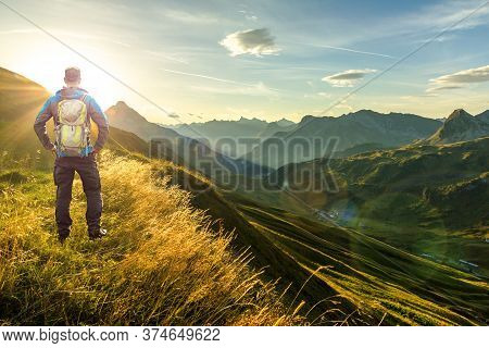 Man Reaching Summit Enjoying Freedom. Beautiful Sunrise And Layered Mountain Silhouettes In Early Mo