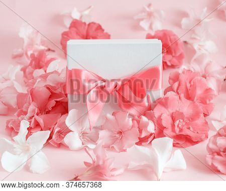 White Gift Box With A Bow Between Pink Flowers Close Up