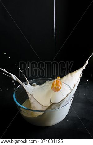 Egg Falling Into A Bowl With Milk And Splashing On A Black Background.