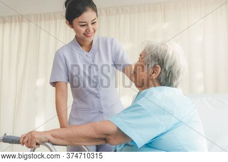 Cheerful Young Nurse In Homecare Helping Senior Patient Use Walker To Recovery From Hip Injury.