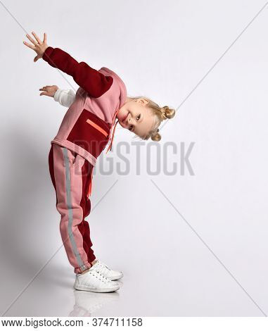 Cute Blonde Schoolgirl In Pink And Red Jym Suit Leaning Head Forward Taking Arms Back. Sports Fashio
