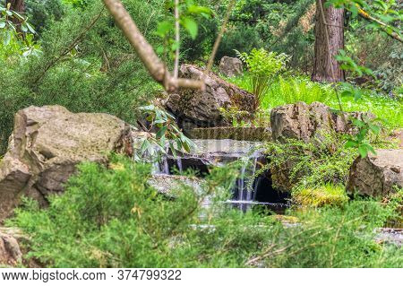 Beautiful Small Waterfall On The River Surrounded By Green Grass On A Cloudy Summer Day