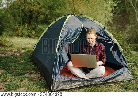 Woman Working On Laptop In Tent In Nature. Young Freelancer Sitting In Camp. Relaxing In Camping Sit