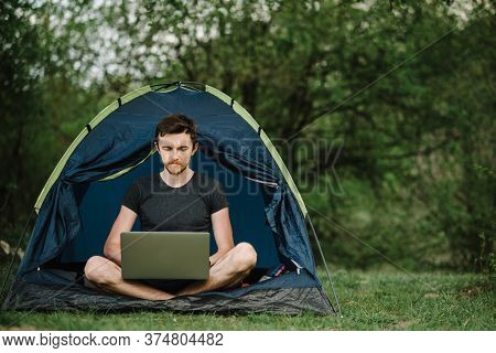 Man Working On Laptop In Tent In Nature. Young Freelancer Sitting In Camp. Relaxing In Camping Site 