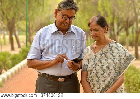 Senior Indian Bengali Couple In Park Looking At Their Smart Phone And Smiling In A Park In New Delhi