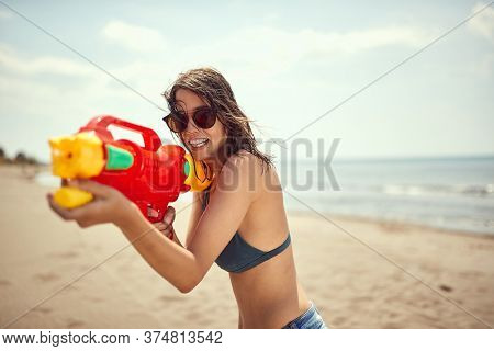 beautiful sexy young female with sunglasses pointing with water-gun on sandy beach