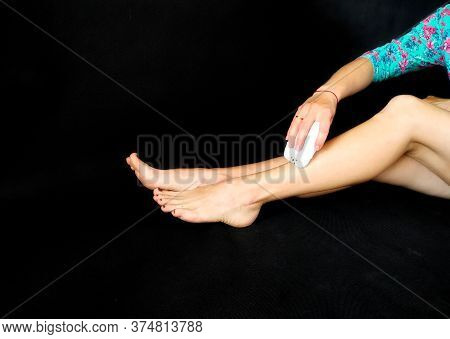 Girl In Makes Hair Removal At Home With White Epilator On Legs At Home. Isolated On Black. Selfcare 