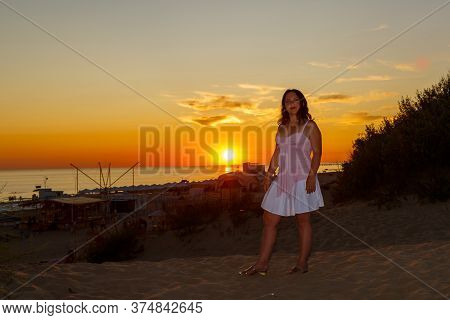 Woman In A White Dress On A Background Of The Sea At Sunset.