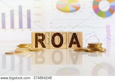 Return On Asset. Roa The Word On Wooden Cubes, Cubes Stand On A Reflective Surface, In The Backgroun