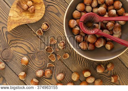 Hazelnuts With A Red Nutcracker In A Bowl On A Wooden Board, Nutshell, Dark Photo, Flat Lay