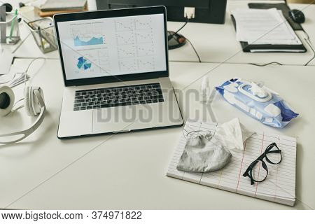 Workplace of modern broker with financial graph and diagram on display of laptop surrounded by sanitizer, mask, eyewear and anticeptic wipes