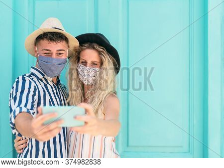 Young Couple Wearing Face Mask Taking Selfie With Mobile Smartphone On Vacation - People Having Fun 