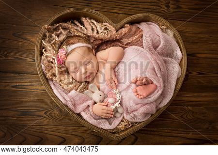 Newborn Baby Girl Sleeping In A Pink Wrap With A White Bandage With A Pink Flower On Her Head. Woode