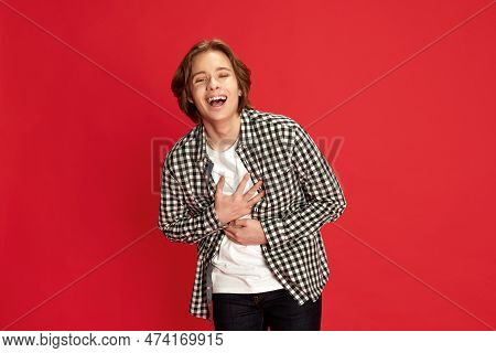 Happy Young Boy Wearing Checkered Shirt And Laughing At Camera Over Red Studio Background. Good Joke
