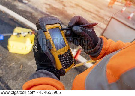 Site Engineer Operating His Touch Screen Controller Instrument During Roadworks. Builder Using Touch