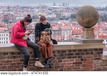 Prague, Czechia - 03.24.2023: Two Ladies Sitting On A Wall Reading Tourist Guides With City Of Pragu