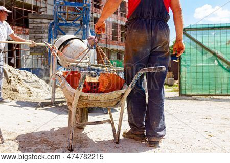 Construction Worker Is Attaching Crane Hooks To Industrial Tipping Barrow Full Of Red Bricks In The 