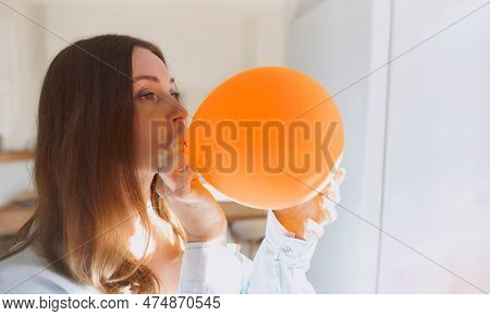 Portrait Of Young Woman Blowing Orange Balloon, Getting Ready To Celebrate Birthday. Home Decoration