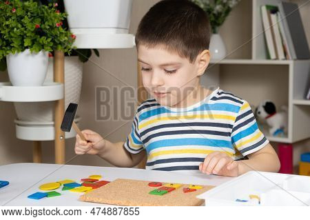 A Preschool Child Plays With A Mosaic, Builds Figures On A Board, Hammering Nails With A Hammer On M