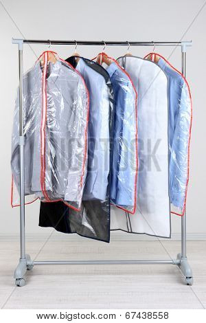 Office male clothes in cases for storing on hangers, on gray background