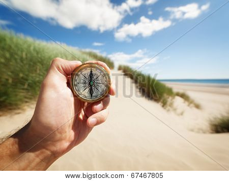 Hand holding a compass on the beach by sea concept for guidance, direction, and adventure