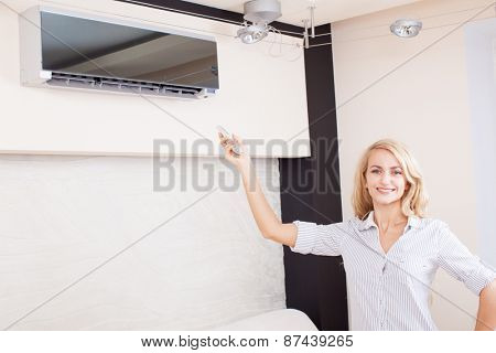 Female holding a remote control air conditioner at home. Happy young woman on sofa