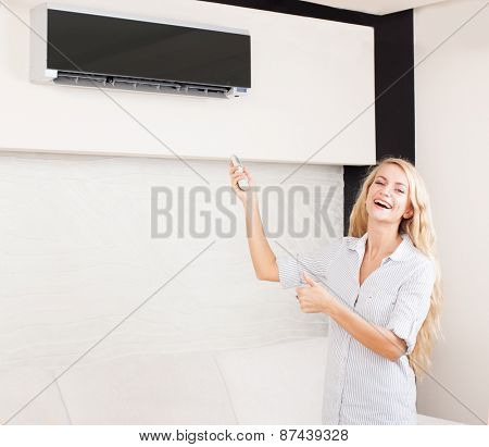 Female holding a remote control air conditioner at home. Happy young woman on sofa