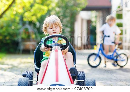 Active Little Boy Driving Pedal Car In Summer Garden