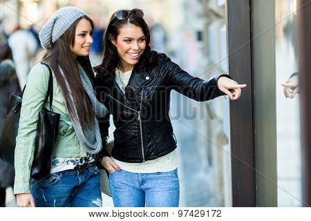 Two Young Women Pointing At A Show-window