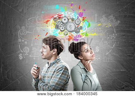 Portrait of a man and an African American woman standing back to back near a blackboard with a colorful brains sketch and cogs on it.