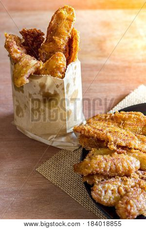 Deep fried sliced banana in paper bag and black dish on wood background