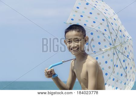 Happy little boy with umbella on the beach at blue sky background.
