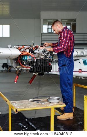 Airplane service crew working on preflight maintenance:  young mechanic fixing turbine of jet plane in hangar